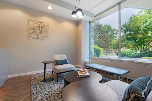 A room with a table, chairs and a bench with a view of trees outside.