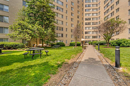 A pathway with a picnic table and a grassy area in front of a building.