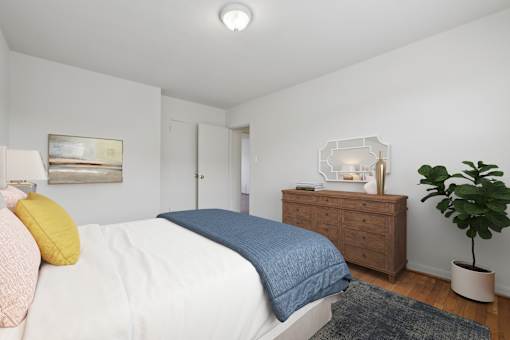 A bedroom with a bed, dresser, and plant.