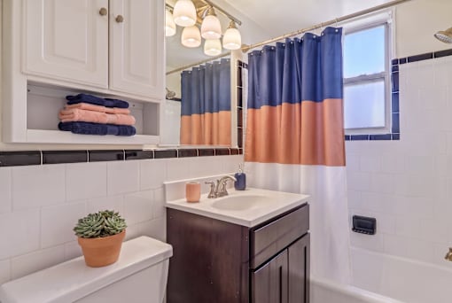 A bathroom with a white toilet, a brown sink, and a window with blue and orange curtains.