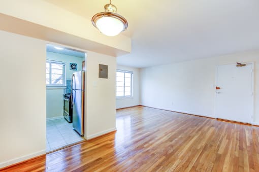 vacant living area with large windows, hard wood flooring and view of kitchen in cambridge square apartments in bethesda md
