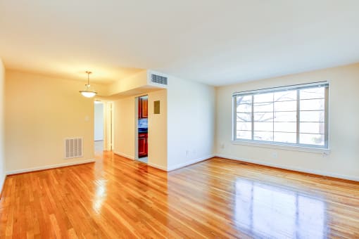 vacant living area with large windows, hard wood flooring and  view of kitchen in cambridge square apartments in bethesda md