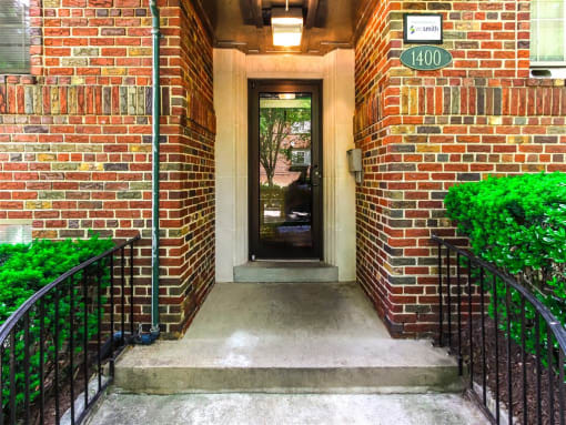 entrance of 1400 van buren apartments with lush landscaping, brick building and sidewalk