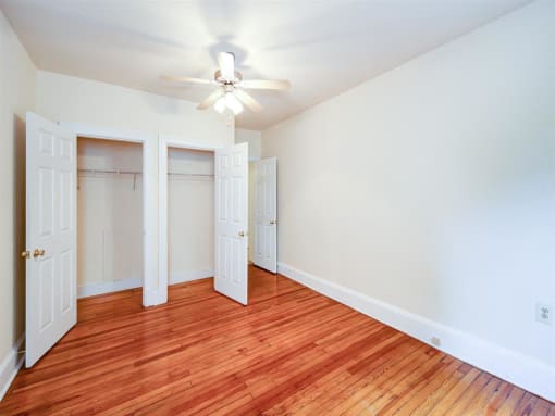 vacant bedroom with hardwood flooring, ceiling fan and large closets at 315 Mount Pleasant apartments in washington dc