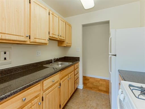 kitchen with tile flooring, refrigerator, gas stove and  oak cabinetry at chillum place apartments in lamond riggs washington dc