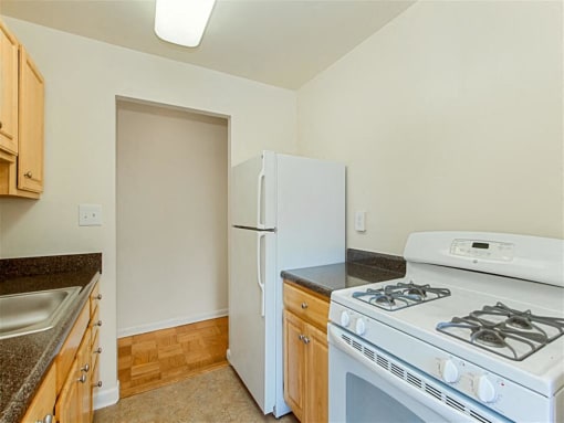 kitchen with tile flooring, refrigerator, gas stove and  oak cabinetry at chillum place apartments in lamond riggs washington dc