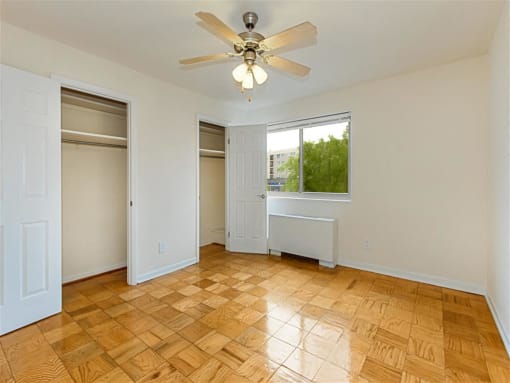 vacant bedroom with hardwood flooring, view of closets, windows, and ceiling fan at chillum place apartments in lamond riggs washington dc