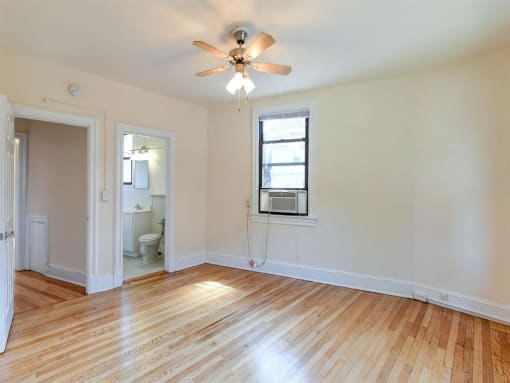 vacant bedroom with hardwood floors, large window, ceiling fan and view of bathroom at the klingle apartments in washignton dc