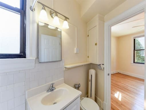 bathroom with vanity, mirror, toilet and view of bedroom at the klingle apartments in washignton dc