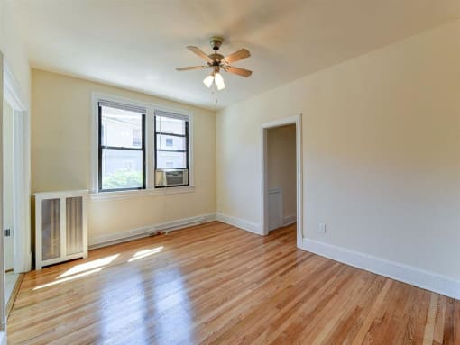 vacant living area with hardwood flooring, large windows and ceiling fan at the klingle apartments in washignton dc