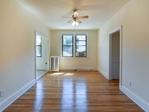vacant living area with hardwood flooring, large windows and ceiling fan at the klingle apartments in washignton dc