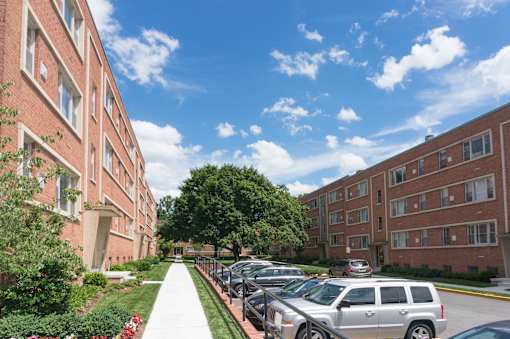 A sunny day at a brick apartment complex with cars parked on the street.