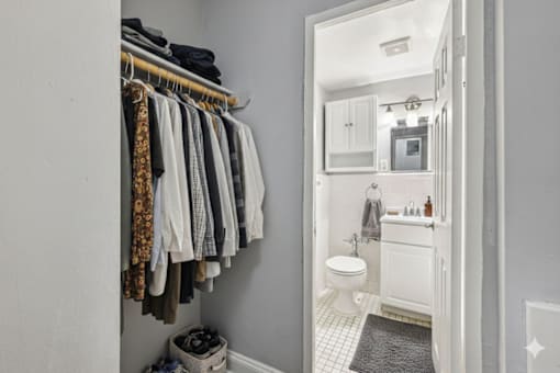 A bathroom with a toilet, sink, and a rack of clothes.