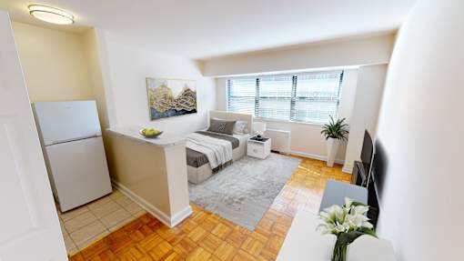 A small, well-lit apartment with a bed, a couch, and a refrigerator.