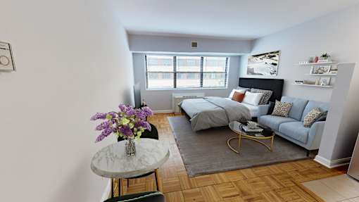 A living room with a grey couch, a round table with flowers, and a window.