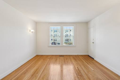 A room with wooden flooring and a window showing a view of a building.