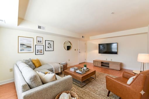 A living room with a grey couch, a brown chair, a coffee table, and a flat screen TV mounted on the wall.