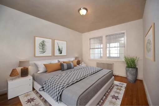 A bedroom with a bed, nightstand, framed pictures on the wall and hardwood floors at the strathmore apartments in downtown bethesda, md.