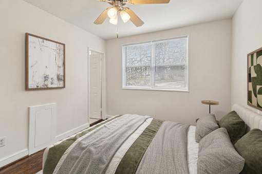 A bedroom with a bed, a ceiling fan, and a window with a view of trees outside.
