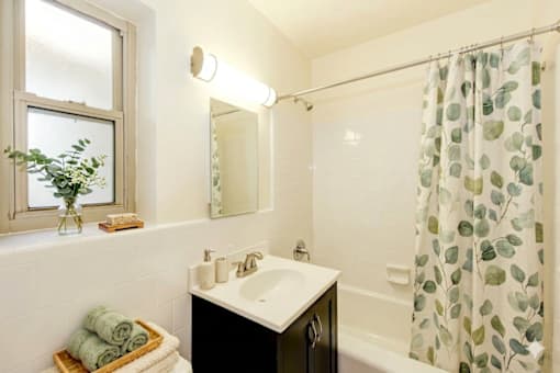A bathroom with a white sink and a shower curtain with green leaves on it.