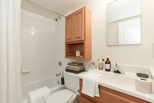 A white toilet sits in a bathroom with a white sink and wooden cabinets.