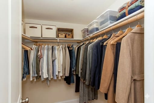 A white closet with clothes hanging and baskets on the shelf.