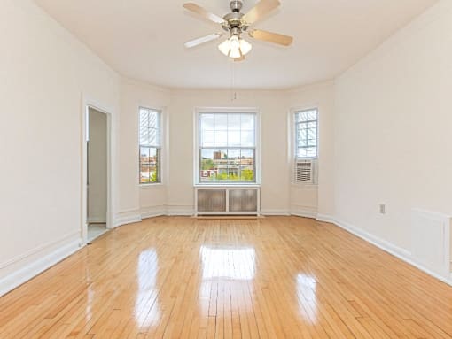 an empty living room with a ceiling fan, hardowod flooring  and three windows at the calverton apartments in washington dc