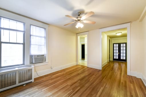 vacant living area with hardwood floors, ceiling fan and view of hallway and sunroom  at  the cortland apartments in washington dc