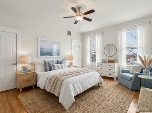 A bedroom with a large bed, a ceiling fan, and a view of the ocean through a window.