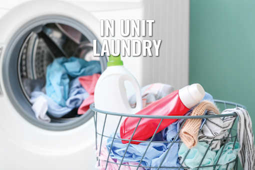 A laundry basket filled with clothes and detergent sits in front of an open washing machine.