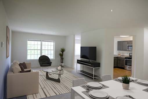 A modern living room with a grey sofa, a black chair, a white coffee table, and a TV on a stand.