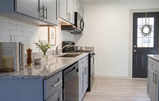 A kitchen with a white brick wall and a black door.
