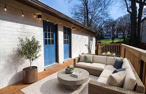 A patio with a white couch, a round table, and a tree in a pot.
