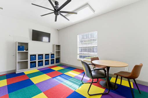 A room with a ceiling fan, a table with chairs, and a television on the wall.