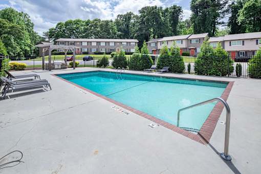 A swimming pool surrounded by a concrete patio and residential buildings.