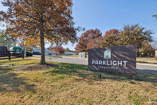 A sign for Parklight Townhomes is displayed in front of a tree with autumn leaves.