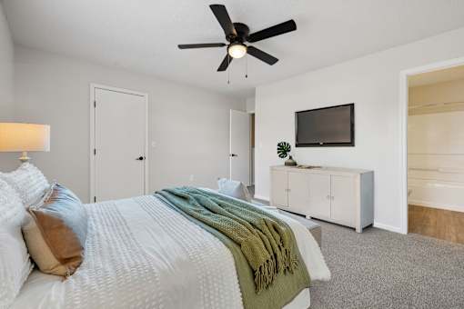 A bedroom with a bed, a ceiling fan, and a television.
