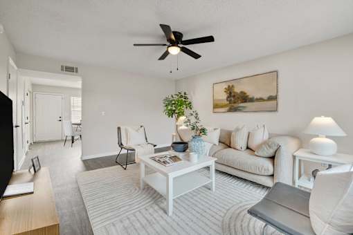 A living room with a white couch, a coffee table, a plant, and a painting on the wall.