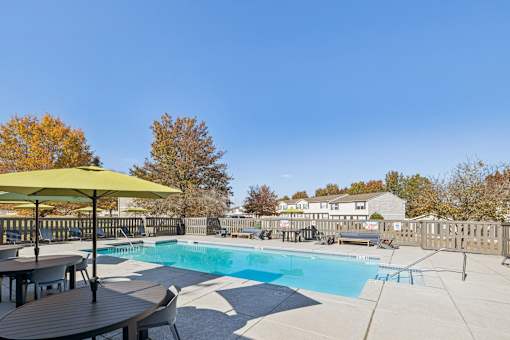 A pool area with a table and chairs and a yellow umbrella.
