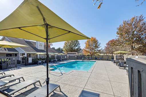 A yellow umbrella is over a table in a poolside area.