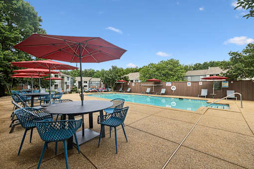 A red umbrella is next to a table with chairs and a pool.