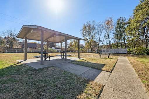A picnic pavilion is situated in a grassy area with a concrete walkway leading to it.