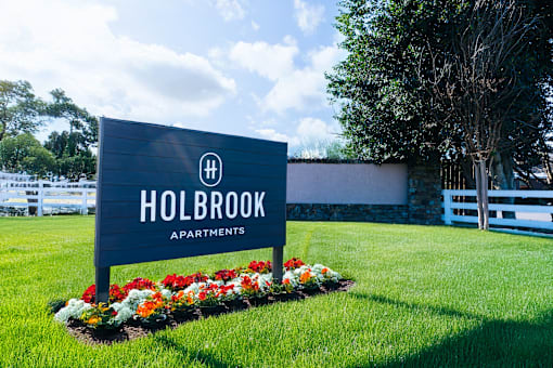 A sign for Holbrook Apartments is surrounded by flowers and greenery.