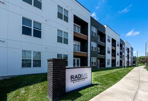 A sign for Radius Apartments stands in front of a row of modern apartment buildings.