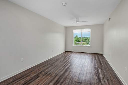 A room with wooden flooring and a window showing trees outside.
