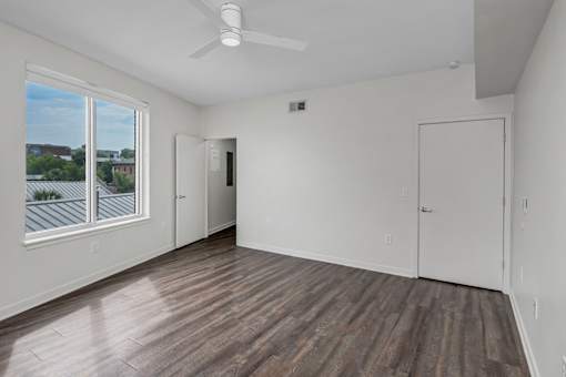 A room with a ceiling fan and a window overlooking a building.