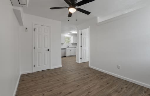 an empty living room with a ceiling fan and a kitchen