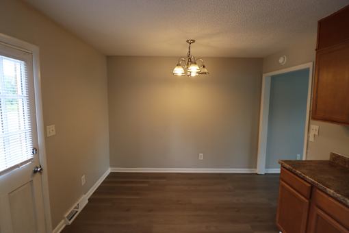 A room with a brown floor and a chandelier hanging from the ceiling.