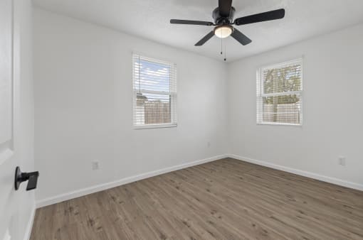 an empty room with a ceiling fan and two windows