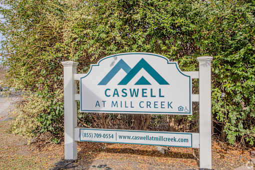 A sign for Caswell at Mill Creek stands in front of a green hedge.